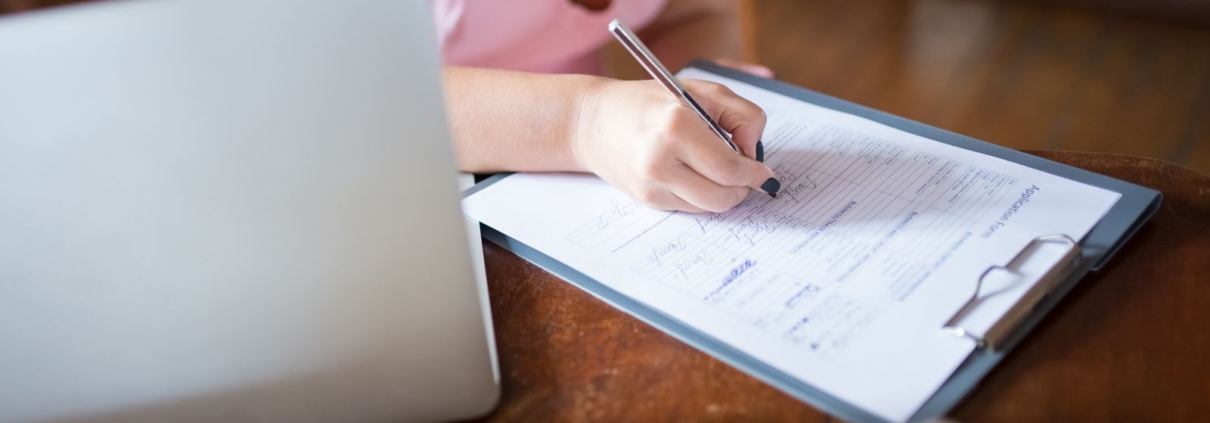 Woman filling in registration forms next to a laptop