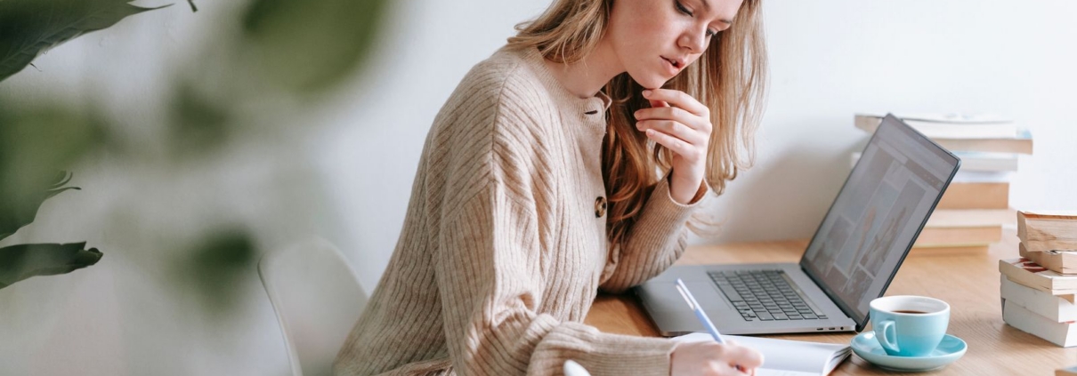 Woman planning at a laptop with coffee while comparing business plan software